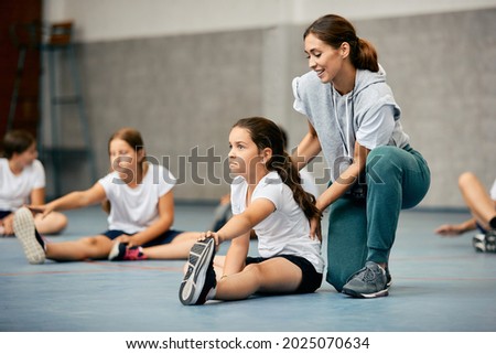 Little girl stretching on the floor and warming up with help of PE teacher during a class at school gym.  Royalty-Free Stock Photo #2025070634