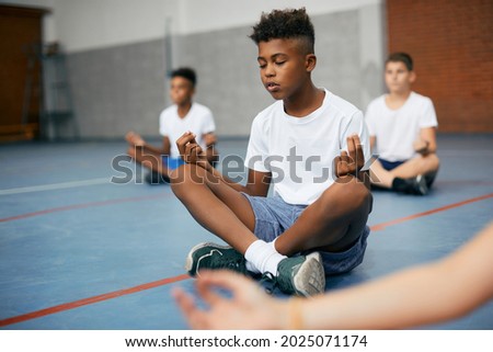 African American schoolboy and his friends meditating in lotus position during PE class at school gym. Royalty-Free Stock Photo #2025071174