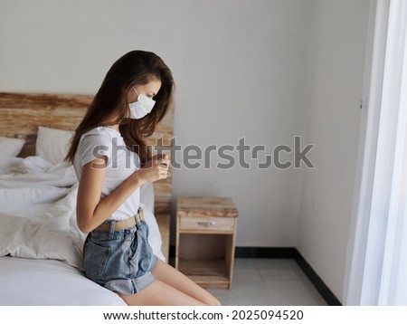 woman on vacation sitting on bed indoors shelf medical mask pandemic quarantine