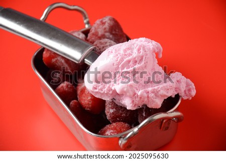Strawberry ice cream with frozen strawberries in silver bowl on red background