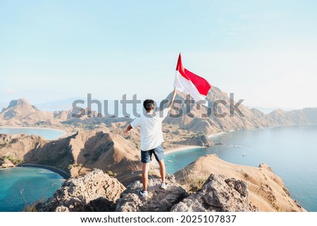 A man holding and waving Indonesian flag on top mountain at Labuan Bajo Indonesia Royalty-Free Stock Photo #2025107837