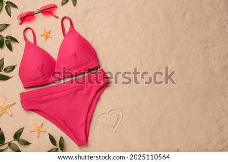 Stylish bikini and beach accessories on sand, flat lay. Space for text