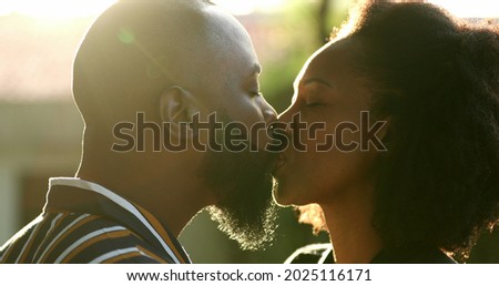 Black man kissing wife outside with lens-flare sunlight. African couple love and affection Royalty-Free Stock Photo #2025116171