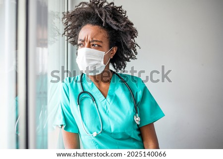Shot of a masked young doctor looking distressed. Tired exhausted female african scrub nurse wears face mask blue uniform gloves sits on hospital. Depressed sad black ethic doctor feels burnout stress