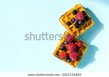 Fresh waffles with different berries of black and red color on a blue background hard light. Homemade cakes crispy waffles on a colored background copy space