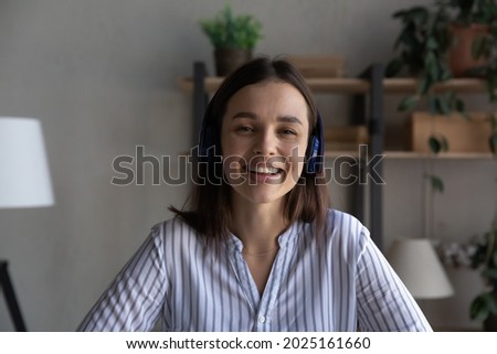 Headshot portrait of smiling millennial Caucasian woman in earphones talk speak on video call at home. Happy young female in headphones have webcam digital virtual event. Communication concept.