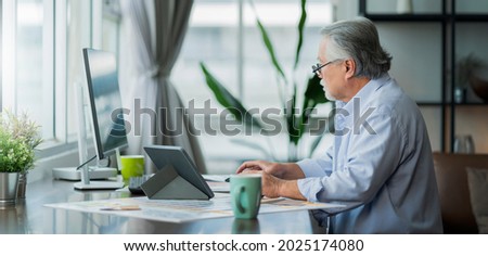 old asian senior retired age working at home hand ise desktop  and paper document at working desk in living room home interior background,asian male senior work at home Royalty-Free Stock Photo #2025174080
