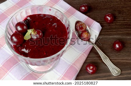 In a vase with cherry jam, which is on a towel, there are several fresh cherries, next to a teaspoon of cherries