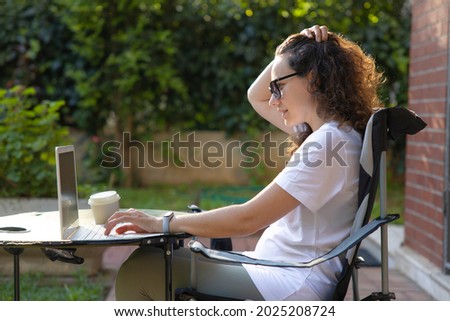 Young woman sitting on a chair in backyard garden and looking at laptop
