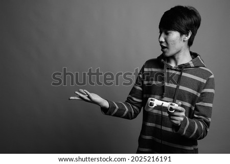 Studio shot of young Asian man playing games against gray background in black and white