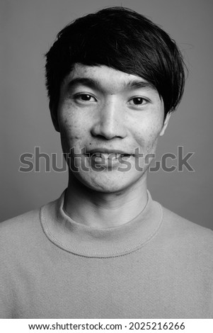 Studio shot of young Asian man wearing sweater against gray background in black and white