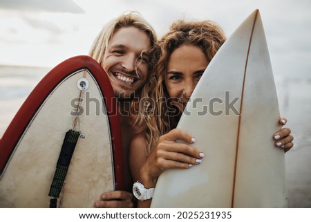 Portrait of optimistic guy and girl hiding behind surfboards Royalty-Free Stock Photo #2025231935