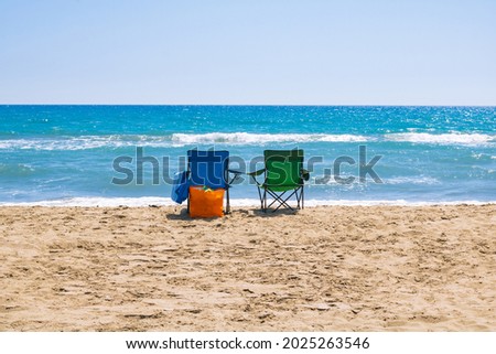 Green and blue camping chairs near the sea on the beach with an orange bag. Holiday, vacation, camping or tourism background photo. 