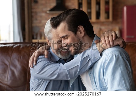 Loving old Caucasian 60s dad hug cuddle adult millennial son show care and support in family relations. Supportive mature father embrace grownup man child, have tender close fatherhood moment. Royalty-Free Stock Photo #2025270167