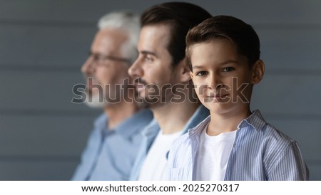 Portrait of happy small teen boy look at camera pose on grey wall background with young Caucasian father and old grandfather. Three generations of men show family unity and boding. Offspring concept. Royalty-Free Stock Photo #2025270317