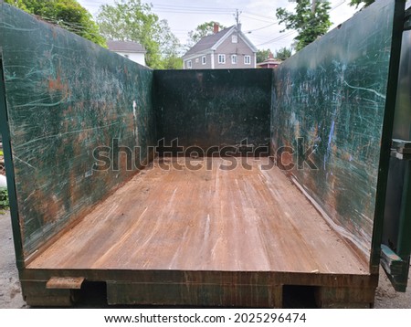 An empty open dumpster sitting in a driveway. The dumpster's walls are covered in scratches and grooves.  Royalty-Free Stock Photo #2025296474