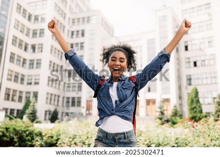 Successful Student. Joyful African American College Girl Shaking Fists Raising Arms After Getting Tuition And Educational Grant For Learning Abroad Posing With Backpack Near University Outside Royalty-Free Stock Photo #2025302471