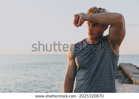 Tired athlete young strong sporty toned fit sportsman man 20s in sports clothes warm up training put hand on forehead at sunrise sun dawn over sea beach outdoor on pier seaside in summer day morning. Royalty-Free Stock Photo #2025320870
