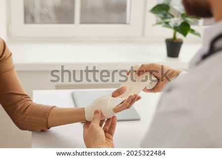 Doctor wrapping young woman's injured hand, close up. Doctor or nurse at modern medical office wrapping patient's sprained wrist with bandage. First aid and professional limb injury treatment concept Royalty-Free Stock Photo #2025322484