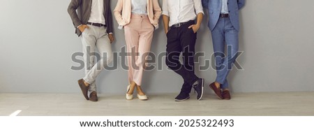 Group of four successful company leaders in classy formal suits standing hand in pocket. Team of 4 business partners leaning on grey office wall. Cropped shot of people's legs in stylish classic pants Royalty-Free Stock Photo #2025322493