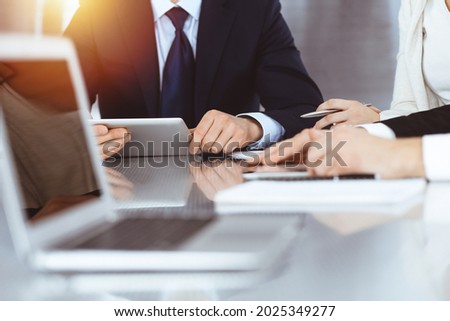 Business people discussing contract while working together in sunny modern office. Unknown businessman and woman with colleagues or lawyers at meeting