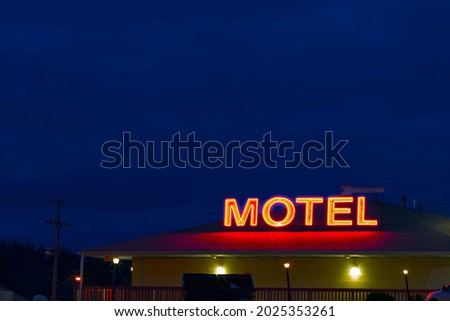 A neon sign reading “MOTEL," glows at dusk with a clear, blue sky in the background. 