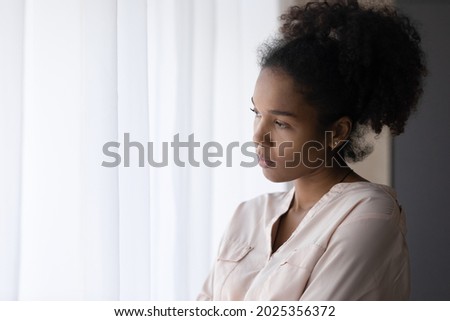 Pensive sad young African American woman look in window distance thinking pondering of life problems. Unhappy mixed race ethnicity female feel lonely lack communication at home. Solitude concept. Royalty-Free Stock Photo #2025356372