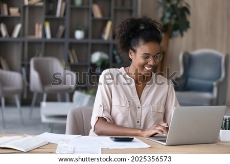 Happy millennial African American woman manage household budget calculate expenses expenditures on machine. Smiling young biracial female pay bills taxes online on computer. Finances concept. Royalty-Free Stock Photo #2025356573