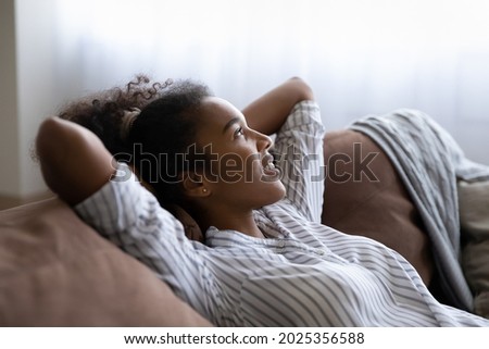 Crop close up of happy calm young African American woman lying on sofa taking nap daydream at home. Smiling millennial ethnic female renter rest relax on couch in living room breathe ventilated air. Royalty-Free Stock Photo #2025356588