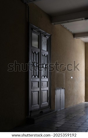 Two mysterious high and large closed patio doors with polygonal glass windows in them in a dark corridor with a wooden shutter in an old building