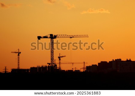 Silhouettes of construction cranes and residential buildings on orange sunset sky background. Housing construction, apartment block in city