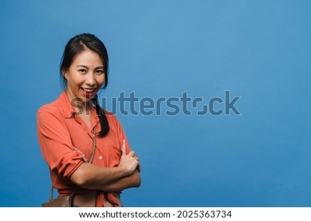 Portrait of young Asia lady with positive expression, arms crossed, smile broadly, dressed in casual clothing and looking at camera over blue background. Happy adorable glad woman rejoices success.