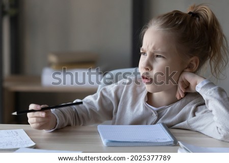 Unhappy little Caucasian girl kid sit at desk feel lazy unmotivated doing homework distressed or bothered with assignment. Upset child lack motivation writing preparing home task. Education concept. Royalty-Free Stock Photo #2025377789