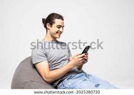 Young man happy positive surprised news comment like use phone sit chair isolated over grey color background