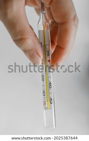 Mercury thermometer in hand, vertical photography.