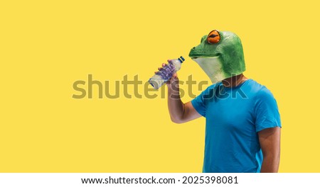 person gesture with frog mask drinking fresh drinking water from a plastic bottle harming the ecology on yellow background with copy space