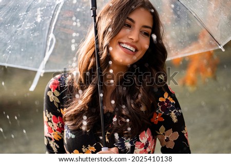 Gorgeous woman smiling and holding umbrella while rain is pouring , closeup shot  Royalty-Free Stock Photo #2025410138