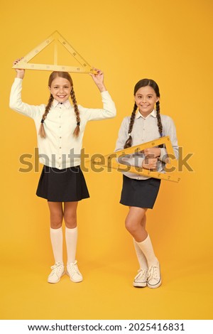Measuring angles at geometry. Cute schoolgirls holding triangles for geometry lesson on yellow background. Little girls learning geometry. Small children with geometrical tools for geometry