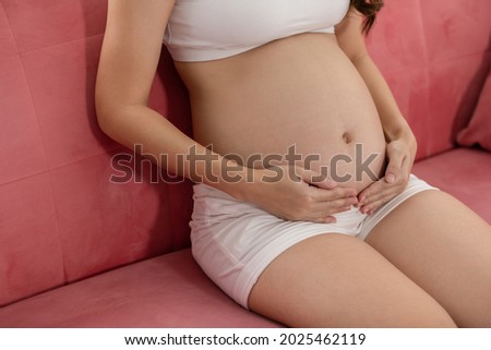 Close up Happy Pregnant Woman sitting on bed holding and stroking her big belly at home,Pregnancy of young woman enjoying with future life relax at home,Motherhood and Pregnant Concept