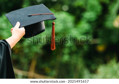 Behind photo of university graduate wears gown and black cap brown tassel