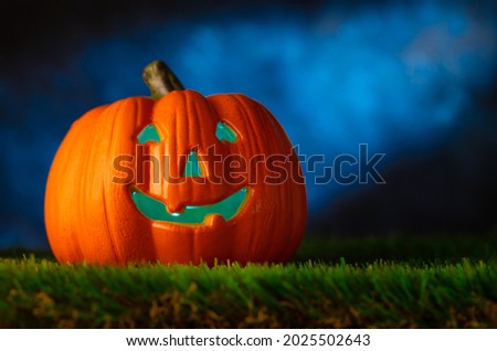 Halloween background. An orange pumpkin in the form of a head on green grass against the background of a dark cloudy night sky. Greeting card, invitation, advertisement, banner, poster.