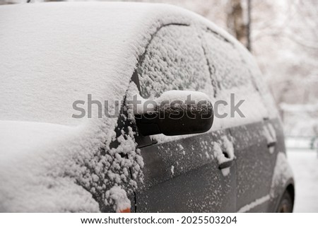 The first unexpected snowfall covered cars with snow. Rearview mirror in the snow. Traffic safety. Selective focus Royalty-Free Stock Photo #2025503204