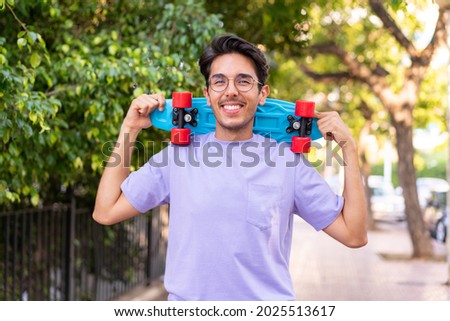Young caucasian man in a park with a skate with happy expression