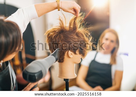 Hairdresser with the Hair Dryer in Hands Teaching Students How to do Hairstyling Royalty-Free Stock Photo #2025516158