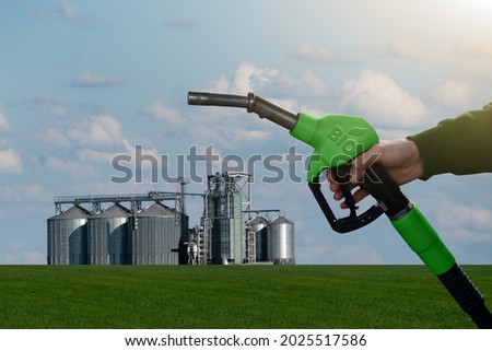 Hand with fuel nozzle with inscription BIO on the background of silos. Biofuel concept Royalty-Free Stock Photo #2025517586