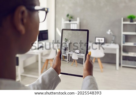 Black rental agent takes photo of apartment interior using smart tablet. Realtor video calling client, showing office workspace, giving tour around new home. Over shoulder device display close up view