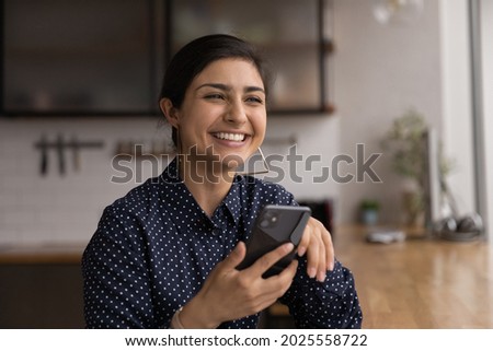 Indian woman sit indoor holding smartphone laughing, read funny media news glad by good news in sms message feels carefree and satisfied. Blogging, new software, funny mobile application user concept