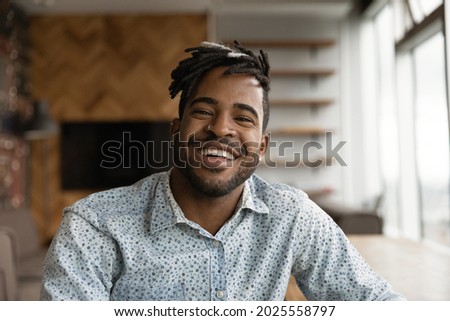 African stylish hipster guy with dreadlocks hairstyle wide toothy smile sit indoor look at camera. Video call event profile picture, portrait of successful entrepreneur pose in modern office concept