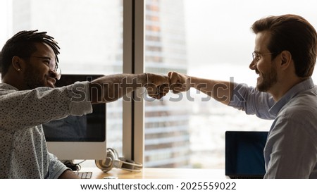 Diverse male colleagues giving fist bump at workplace. African guy greeting Caucasian mate, symbol of business partnership, racial equality, friendship at work. Respect, support, collaboration concept Royalty-Free Stock Photo #2025559022