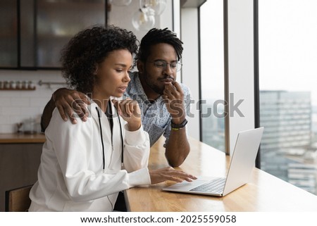 African couple spend time in kitchen, wife sit at bar counter use laptop discuss with husband purchase on e-commerce services, browse internet, search information, buy tickets online remotely concept